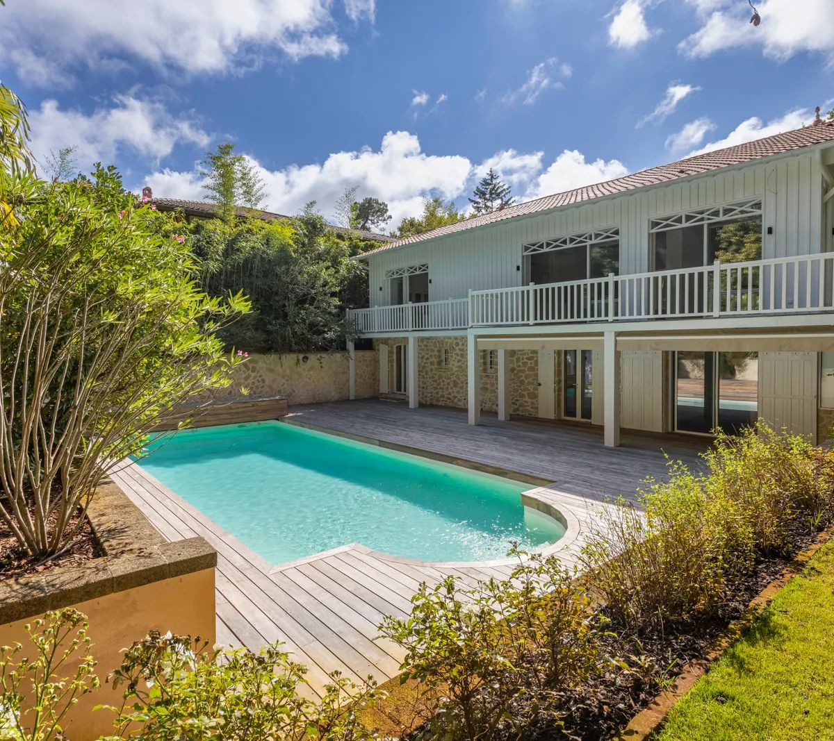 Maison moderne rénovée avec piscine, terrasse en bois et jardin tropical luxuriant sous ciel bleu