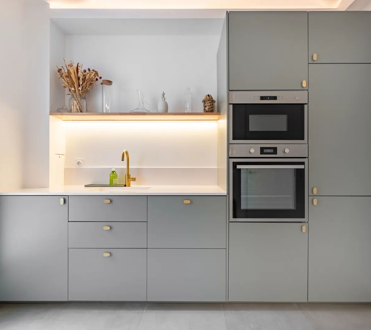 Cuisine moderne grise avec électroménager encastré, plan de travail blanc, éclairage LED et robinet doré