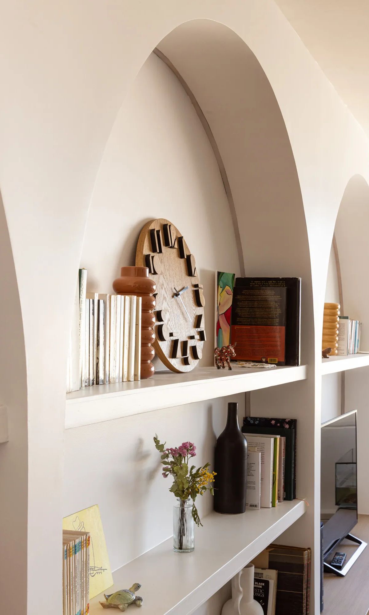 Étagères encastrées dans alcôve arquée blanche avec livres et objets déco, aménagement intérieur moderne