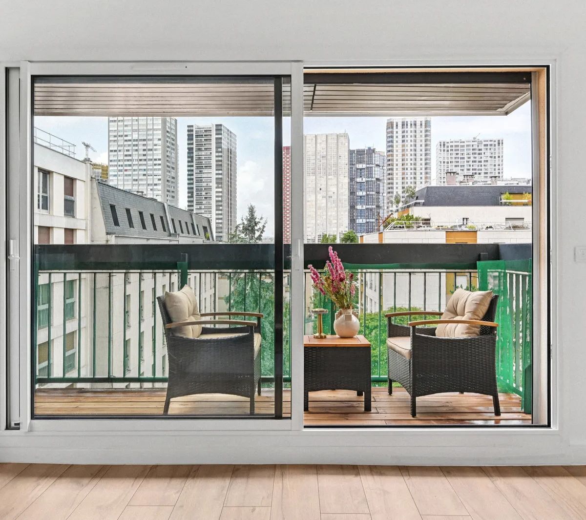 Balcon moderne avec mobilier d'extérieur et vue sur immeubles urbains depuis baie vitrée coulissante