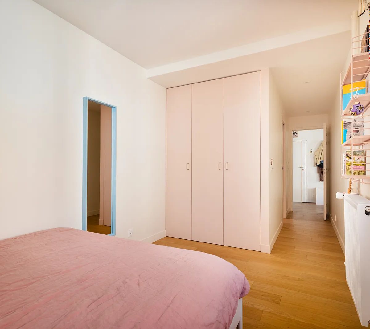 Chambre moderne avec dressing rose intégré, parquet en bois et mur d'accent coloré, design contemporain et fonctionnel