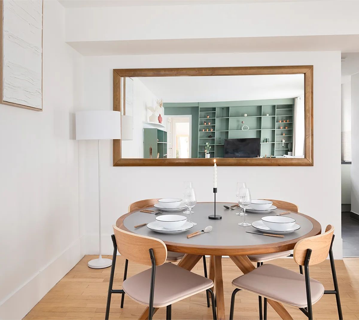 Salle à manger moderne avec table ronde en bois, chaises design et miroir encadré, cuisine ouverte en arrière-plan
