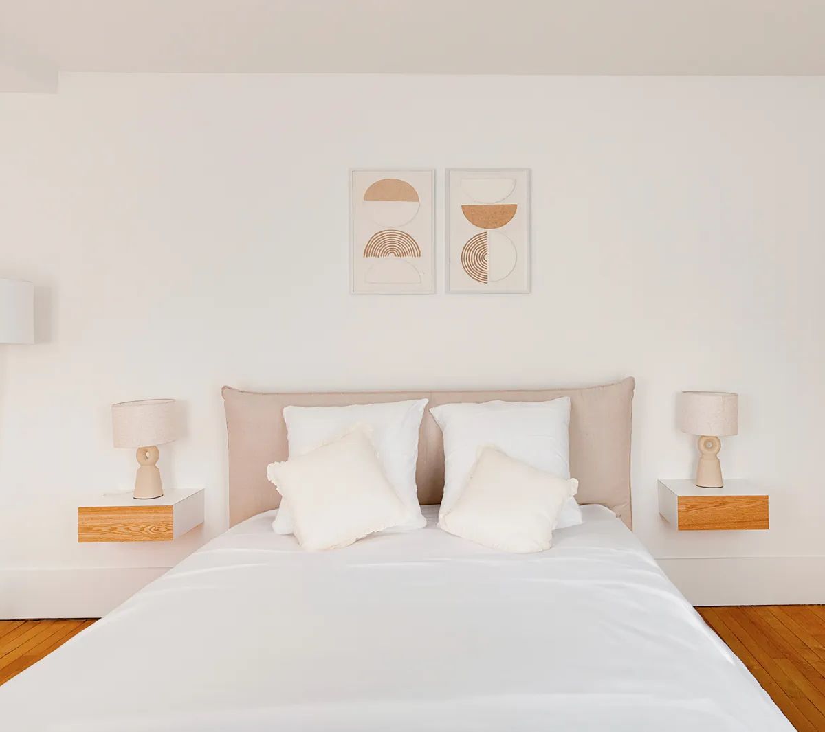 Chambre moderne minimaliste avec lit beige, parquet bois, tableaux géométriques et éclairage design sur murs blancs